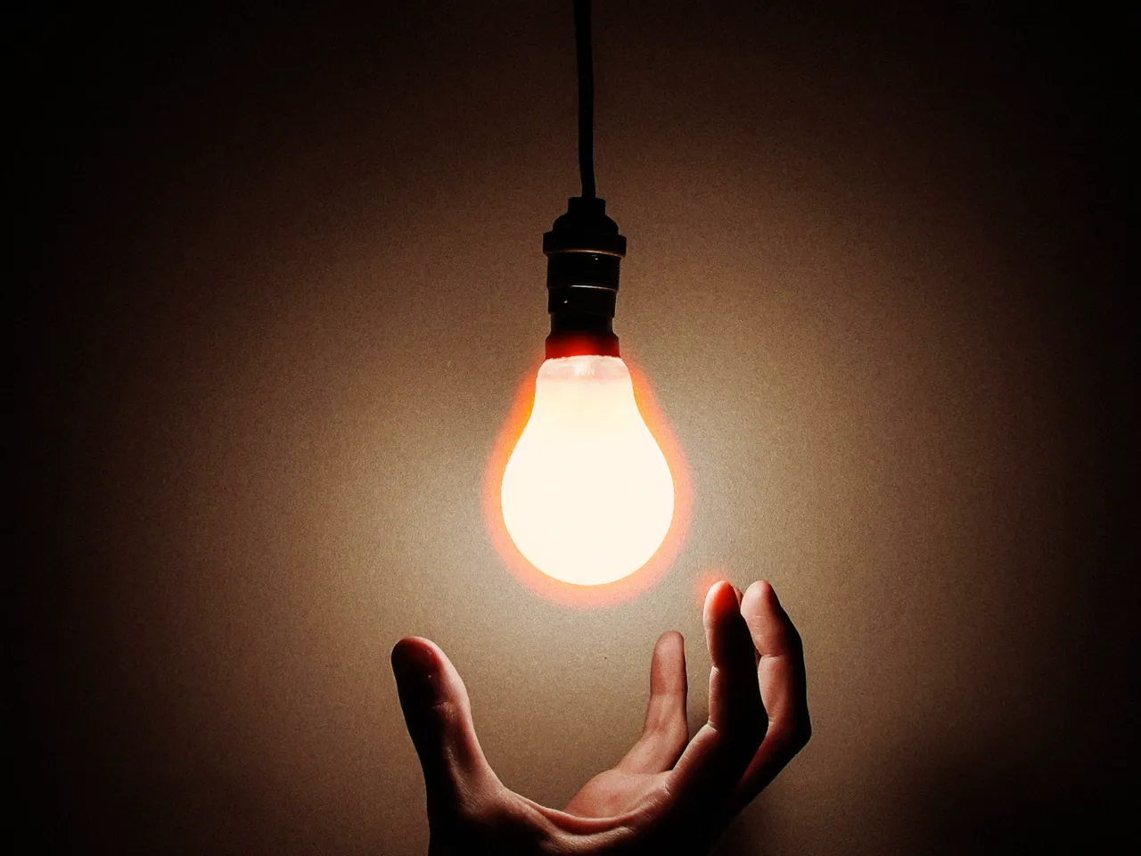 A bare light bulb hanging in a dark room, glowing above an open hand, with halation at 50%